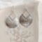 Close-up of sterling silver pear-shaped hammered dangle earrings with French hook ear wires on a marble surface.

